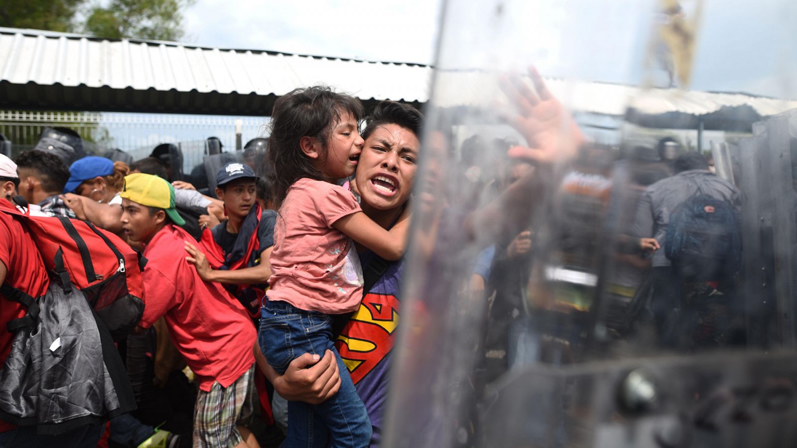 Un migrante hondureño con una menor en brazos grita hacia policías mexicanos en el paso fronterizo con Guatemala