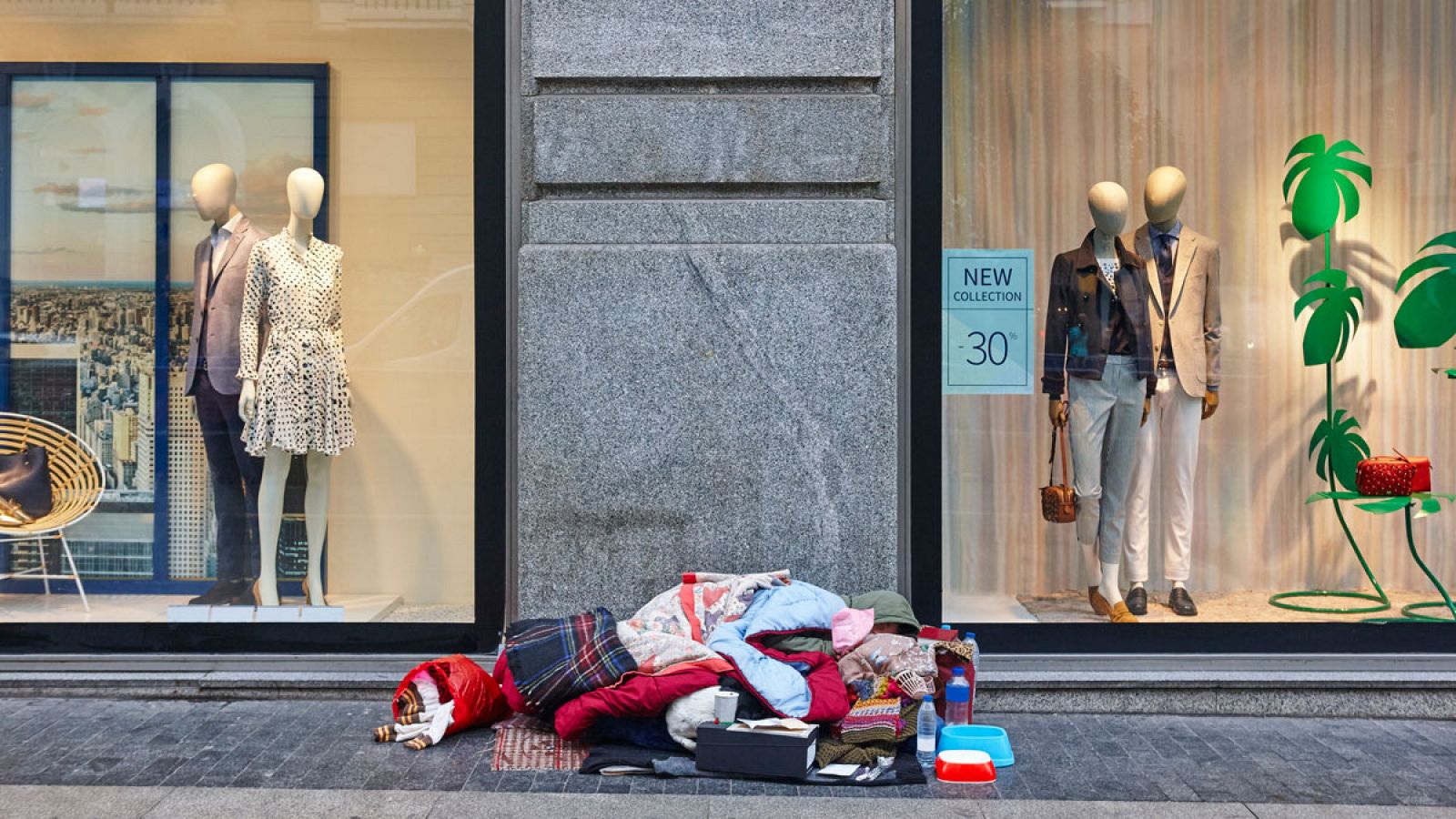 Una mujer duerme en la acera de una gran ciudad bajo los esaparates de una tienda de moda.