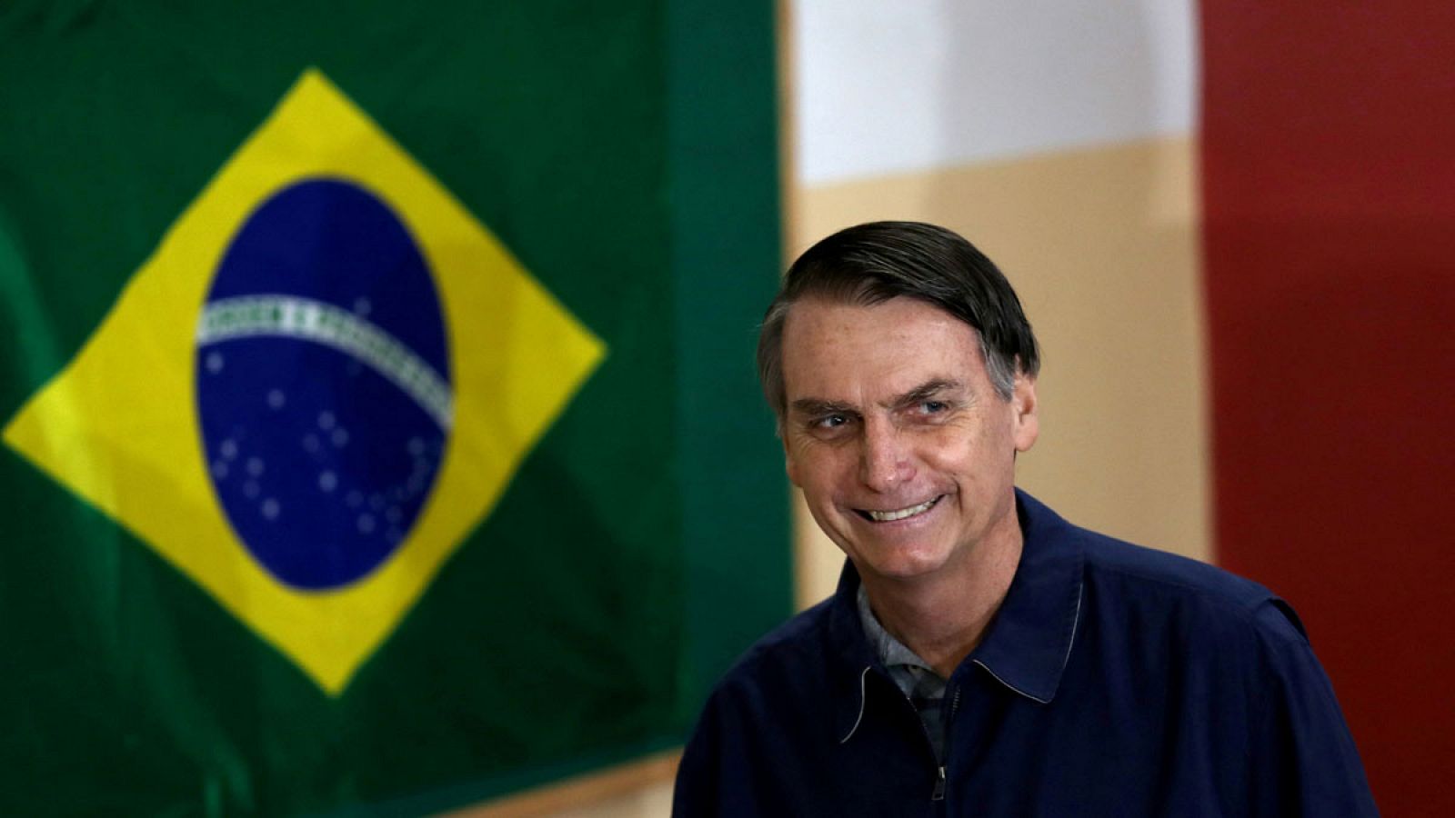 El candidato de extrema derecha, Jair Bolsonaro, pasa delante de una bandera de Brasil.