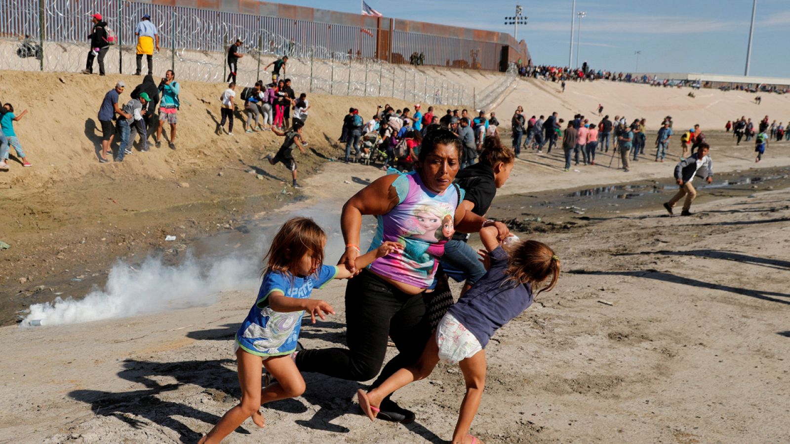 Una mujer hondureña huye del gas lacrimógeno junto a sus hijas en la frontera con México