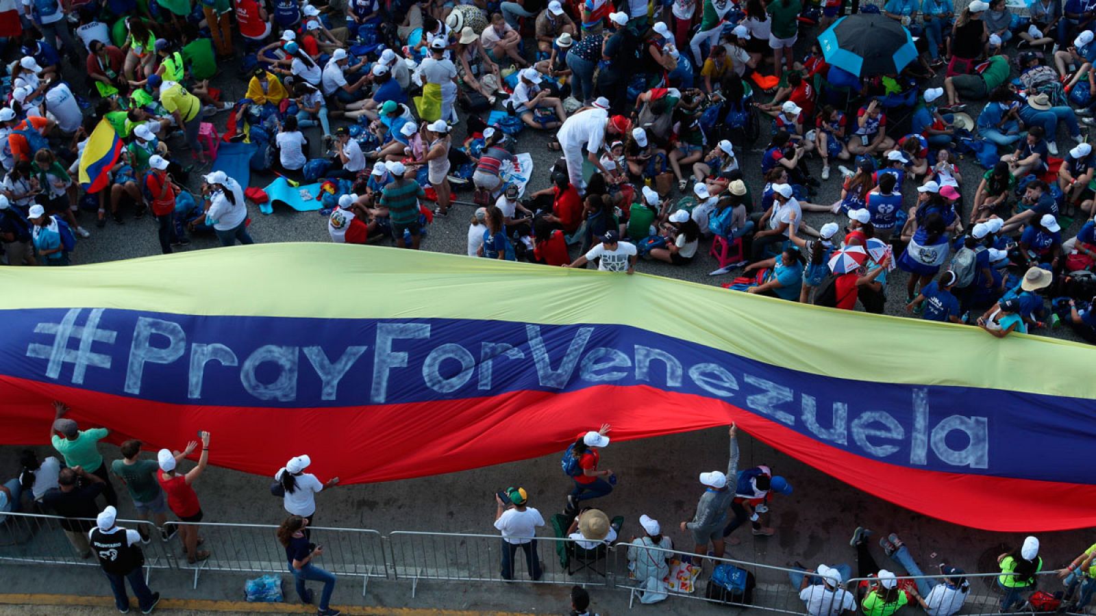 Jóvenes peregrinos de la JMJ con una gran bandera venezolana en la que se lee "Pray for Venezuela"