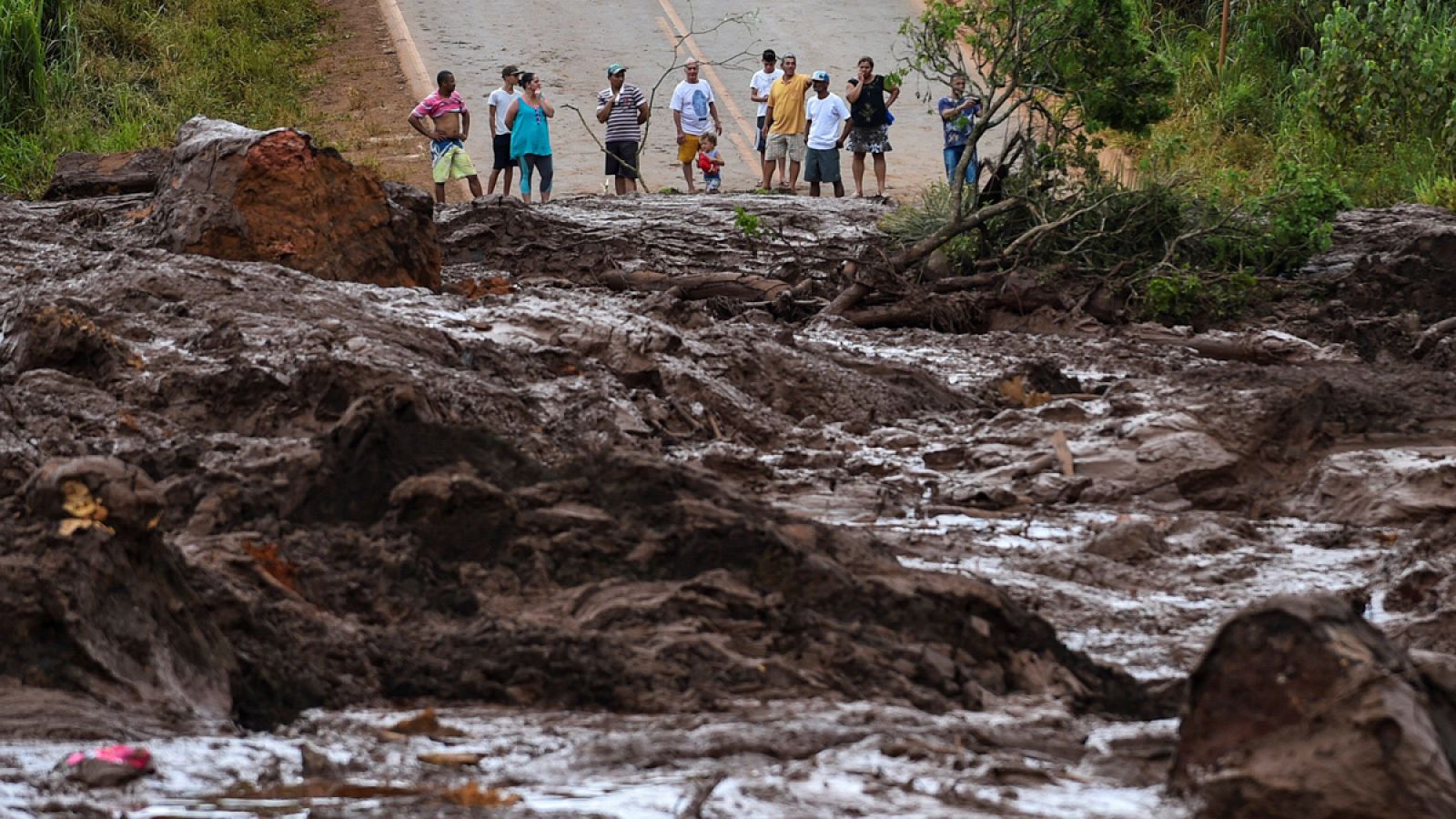 Un grupo de personas observa el desastre causado por la rotura de una presa que contenía residuos minerales de la compañía Vale