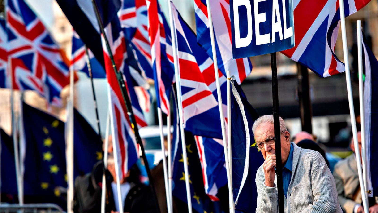 Un hombre se recosta pensativo ante el Parlamento de Westminster, rodeado de banderas británicas y europeas