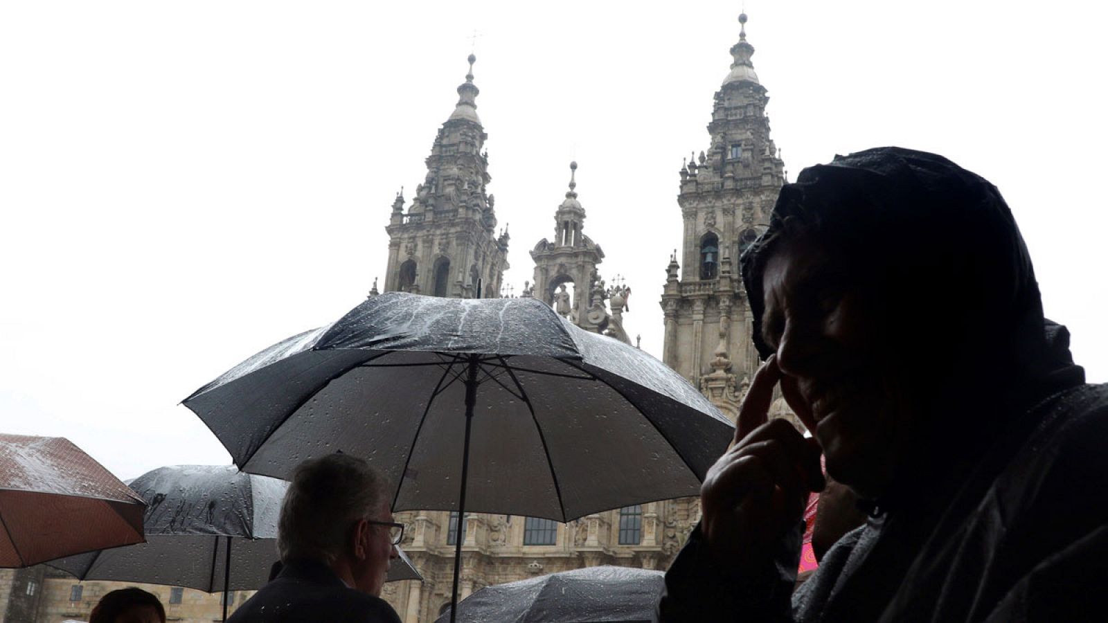 Peregrinos y turistas se protegen del viento y la lluvia en la zona vieja de Santiago de Compostela.