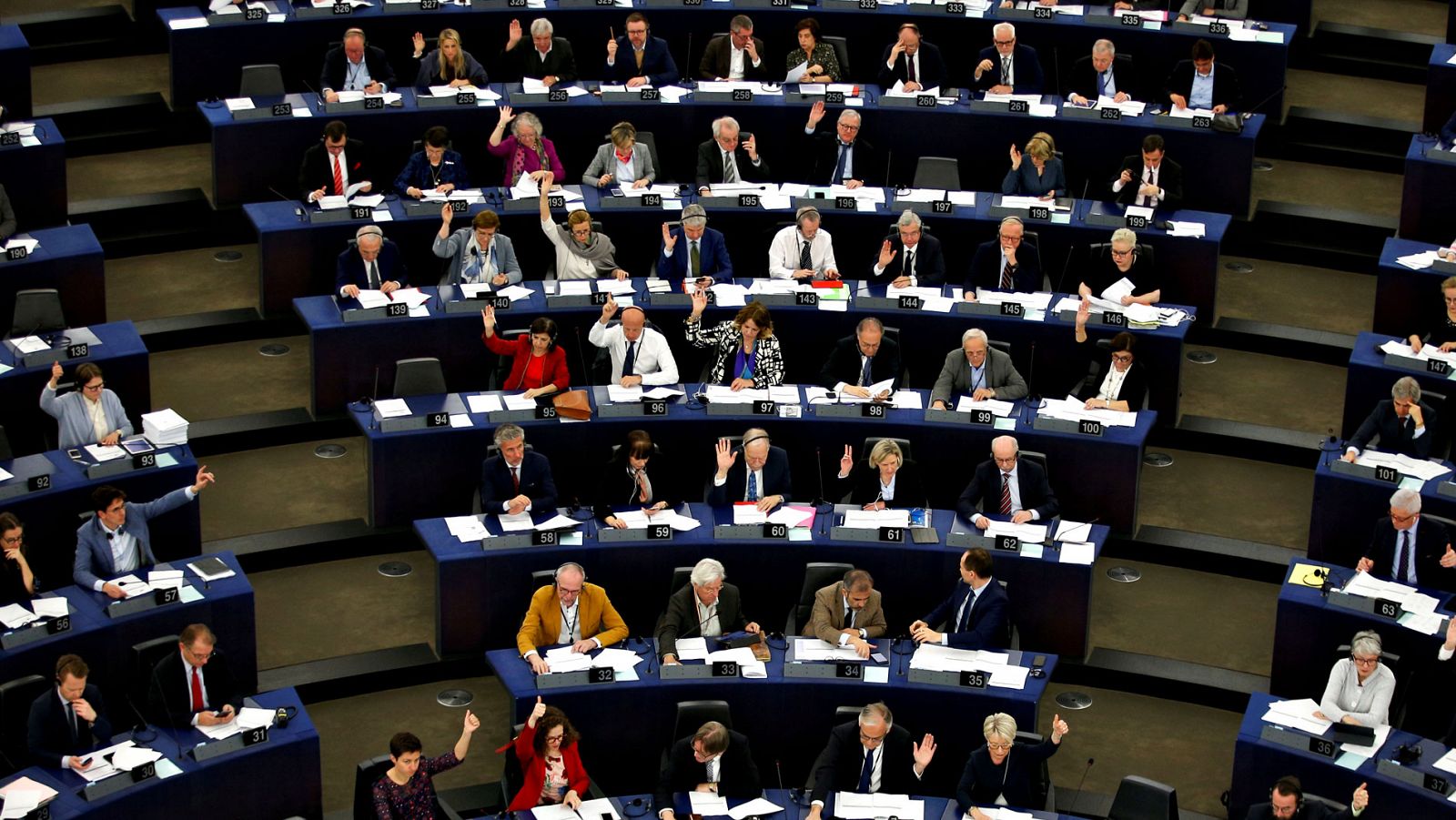 Varios diputados votan a mano alzada en el Parlamento Europeo