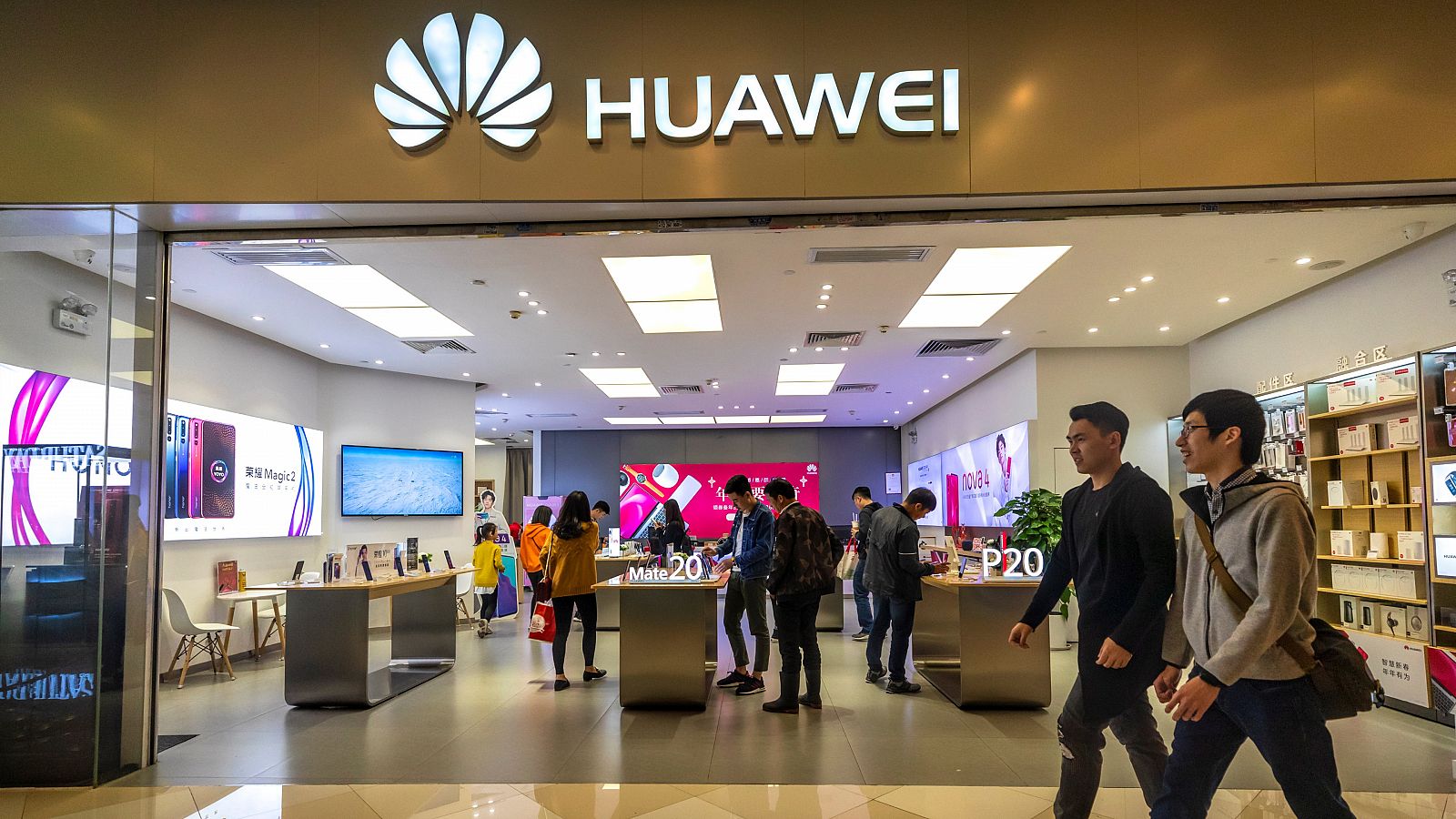 Dos hombres caminan frente a una tienda de Huawei.