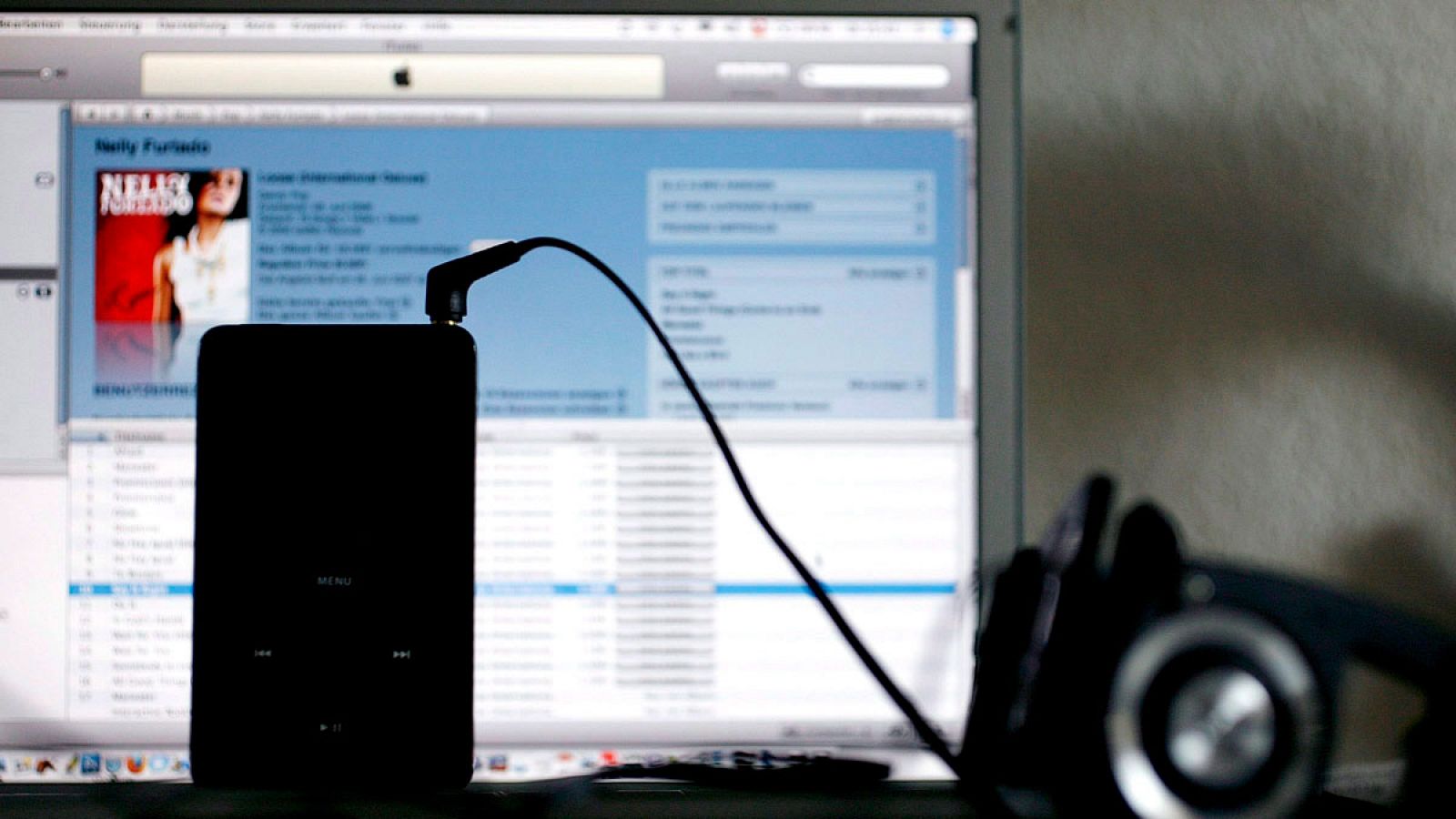 Fotografía de archivo en la que se observa un reproductor de música iPod frente a un "iTunes Music Store" en un ordenador portátil.