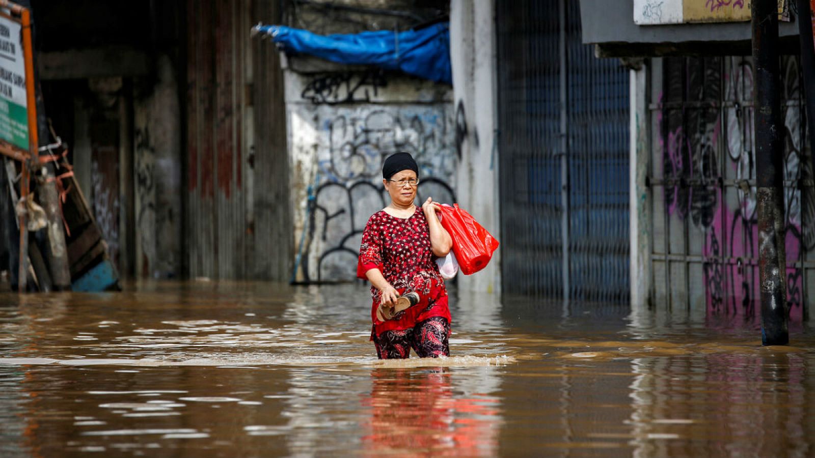 En la imagen, una mujer carga con sus pertenencias en medio de una gran riada.