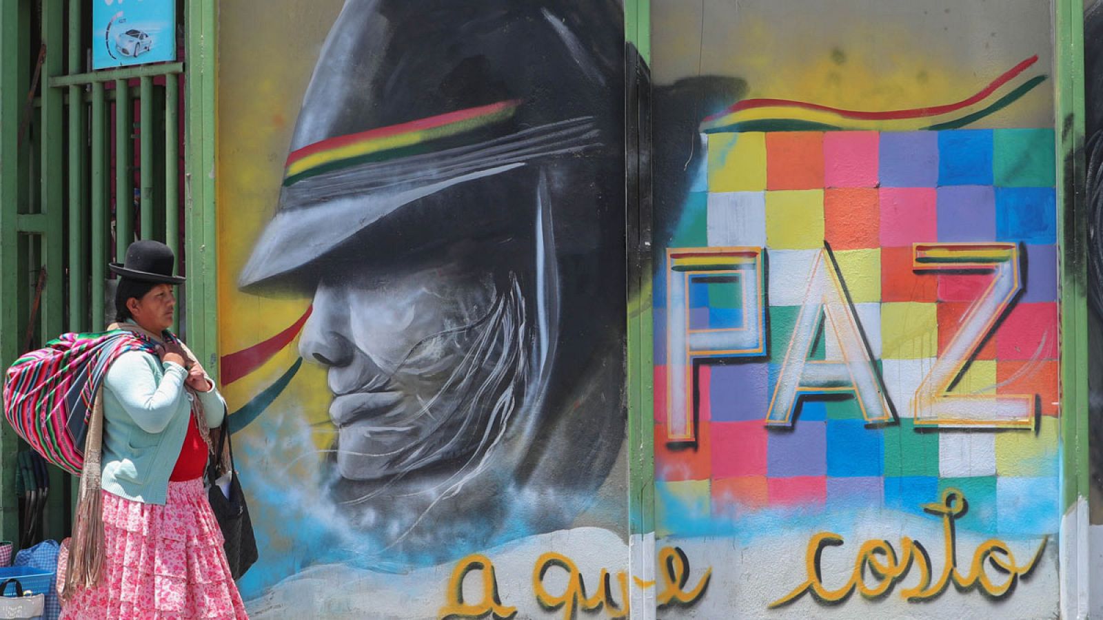 Una mujer boliviana caminando frente a un mural artístico en La Paz.
