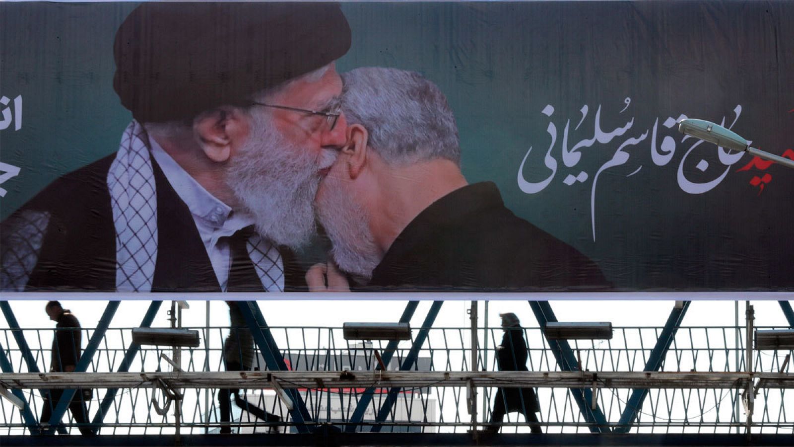 Viandantes cruzan un paso elevado en el que se muestra un cartel del ayatolá Alí Jamenei (izq), abrazando a Soleimani