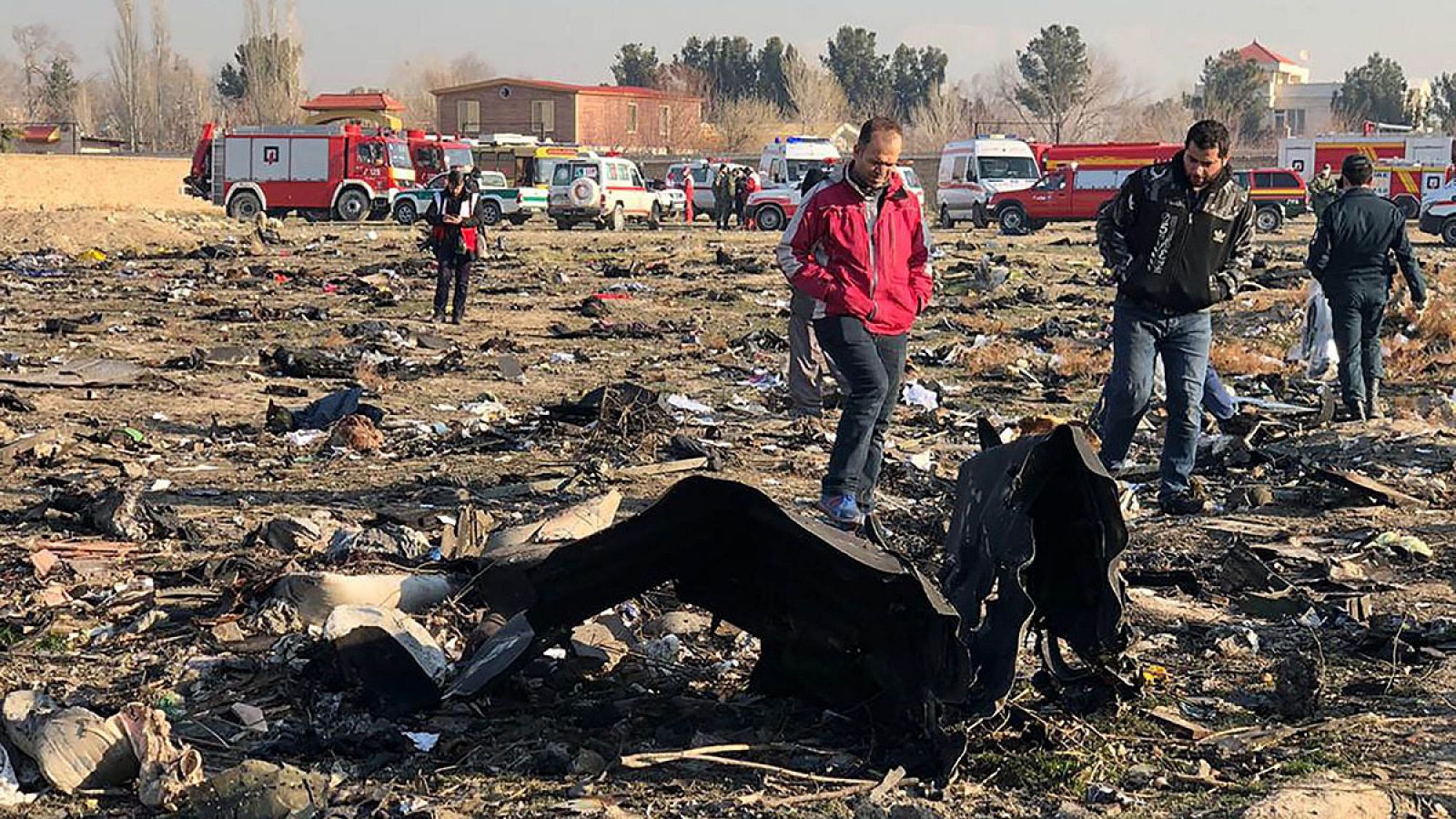 Un grupo de gente camina junto a los restos del avión ucraniano derribado el miércoles en Teherán.