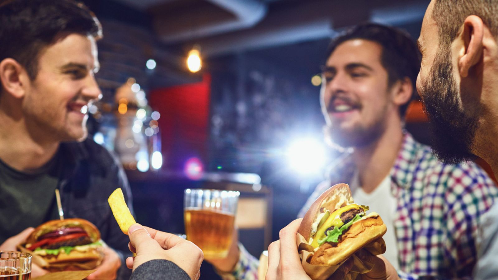 Un grupo de amigos come hamburguesas y bebe cerveza en un bar