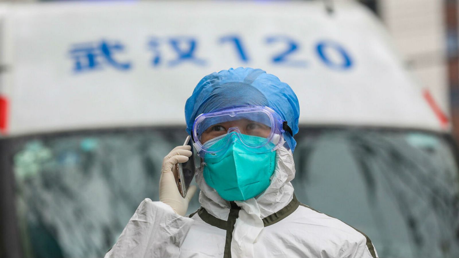 Una enfermera completamente protegida atiende una llamada junto a una ambulancia en Wuhan, origen del brote.