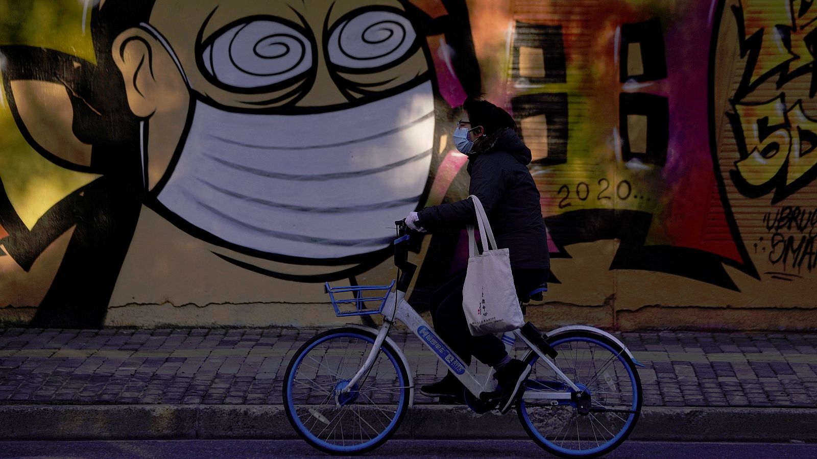 Un ciclista pasa por delante de un mural pintado en una calle de Shanghai.