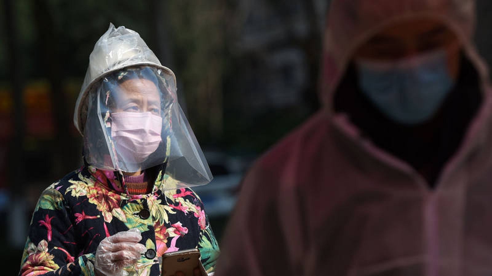Dos personas con mascarilla esperando a recoger provisones en un complejo residencial de Wuhan, China.  