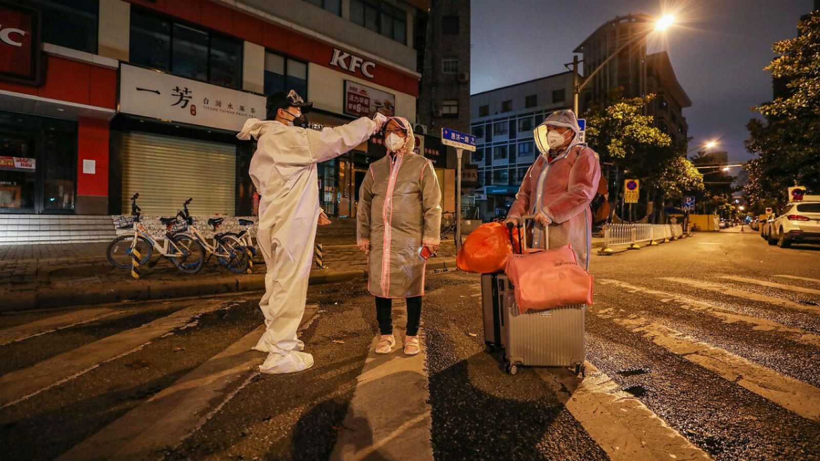 Un voluntario toma la temperatura y a acompaña a dos personas, una de ellas embarazada, al hospital de Wuhan.