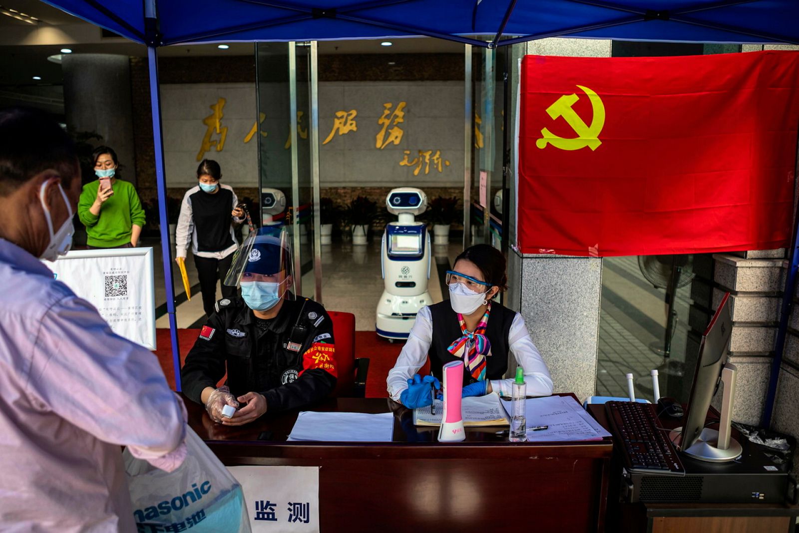 Dos personas comprueban la temperatura corporal de los visitantes en Guangzhou con ayuda de un robot