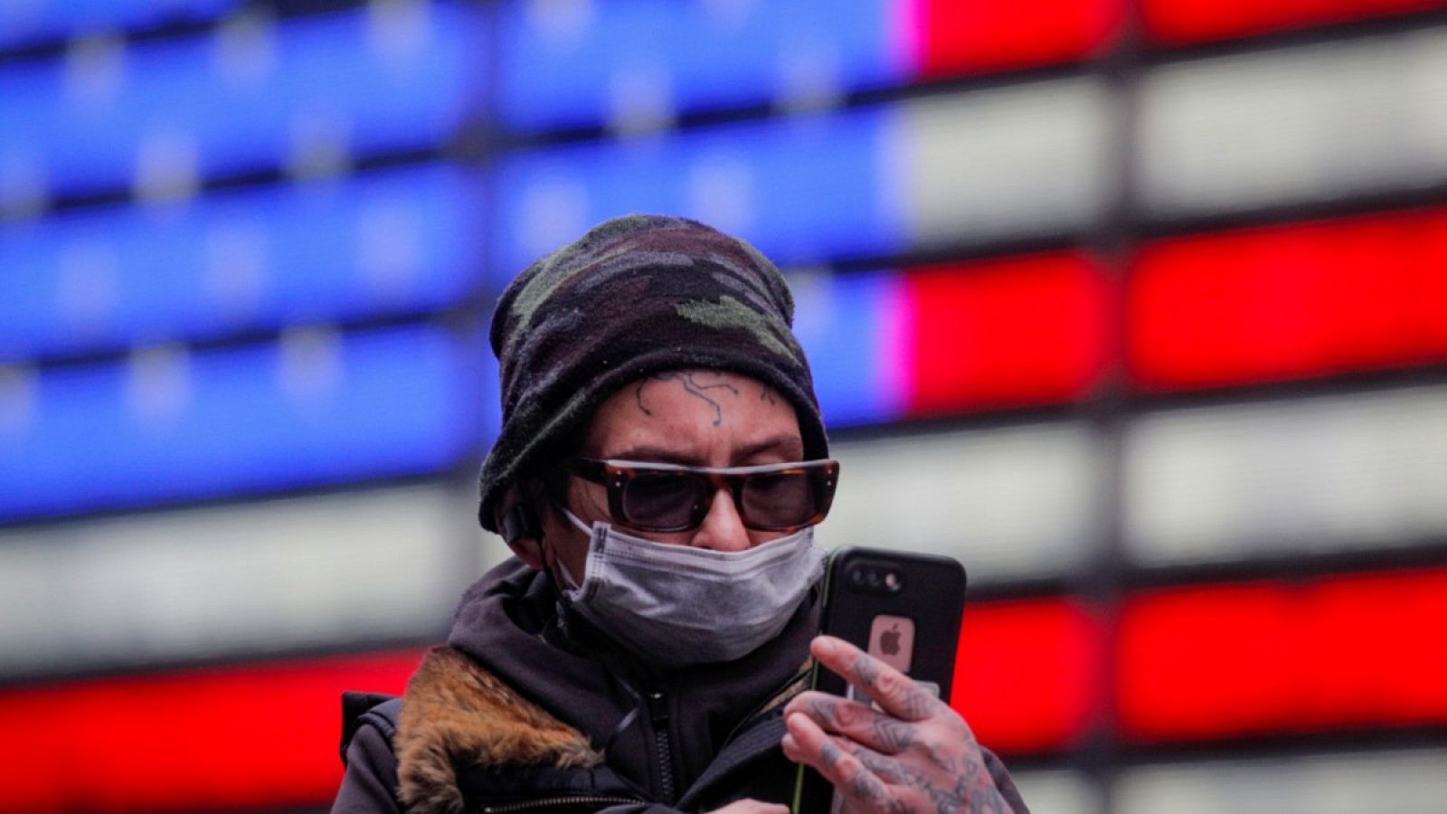 Un hombre con mascarilla mirando su móvil mientras camina por Times Square.