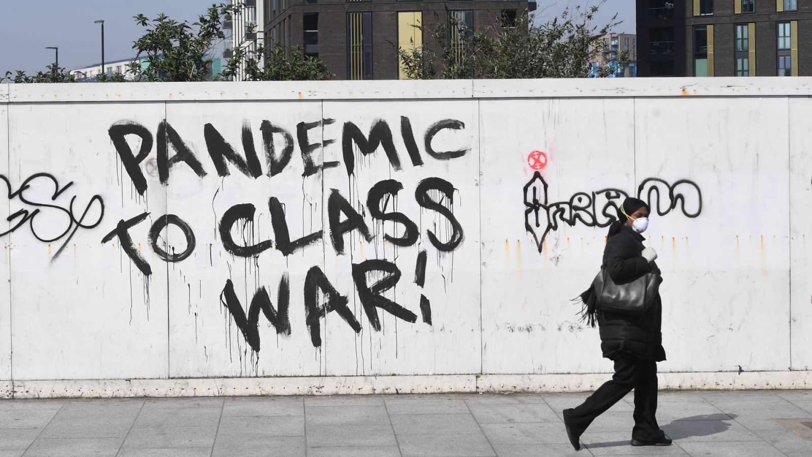 Una mujer con mascarilla pasa junto a un grafiti en Londres (Reino Unido)