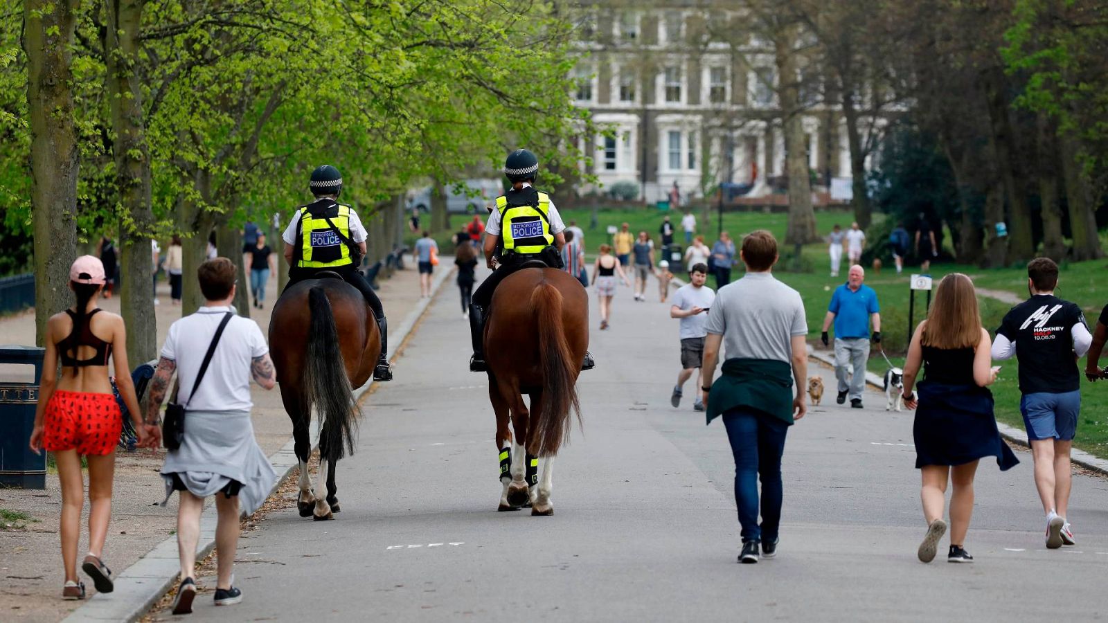 Personas de paseo y patrulla de policías a caballo en un parque de londres, este sábado