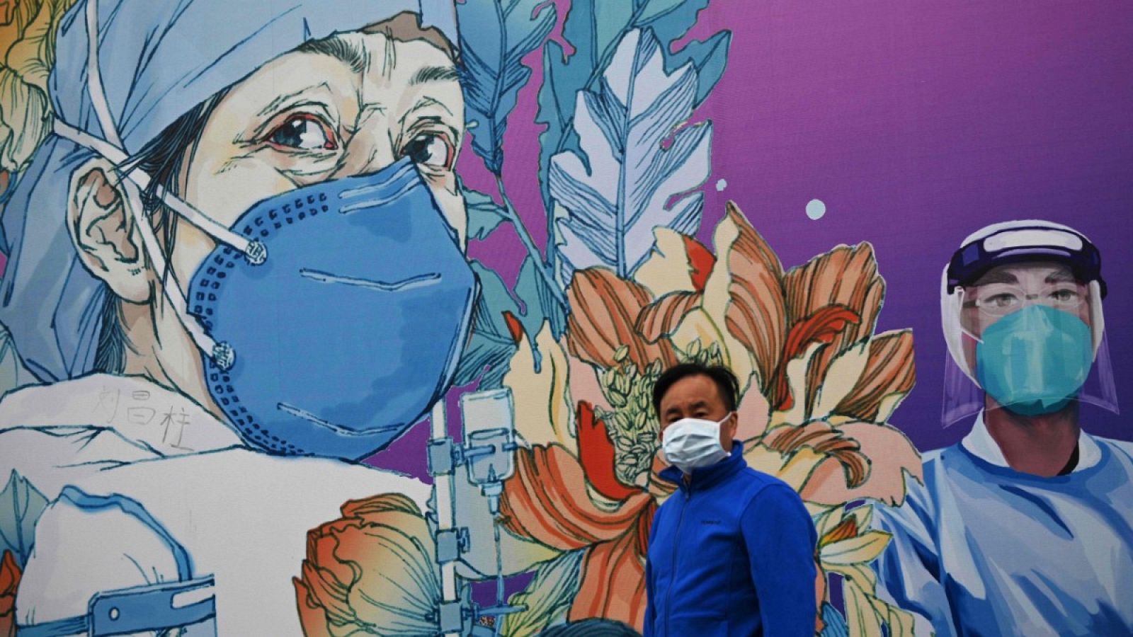 Un hombre con mascarilla caminando frente a un mural en el Hospital Leishenshan en Wuhan.