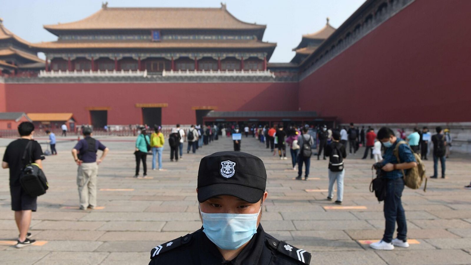 Un guardia vigila que la gente hace cola manteniendo la distancia de seguridad (Pekín)