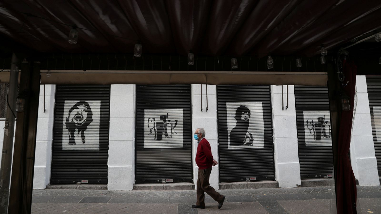 Un anciano pasa por delante de un restaurante cerrado