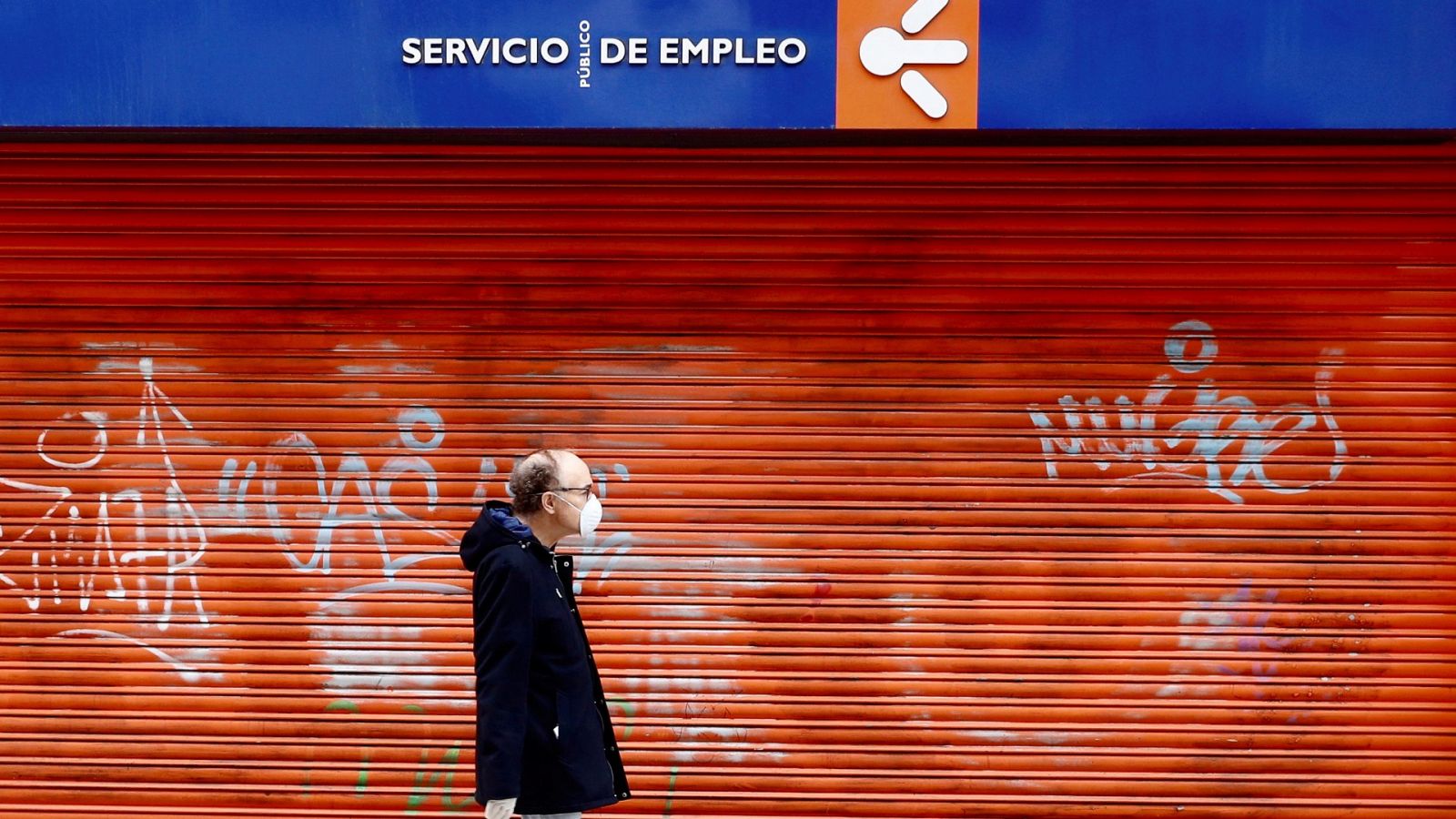 Un hombre con mascarilla camina en frente a una oficina de empleo cerrada en Oviedo.