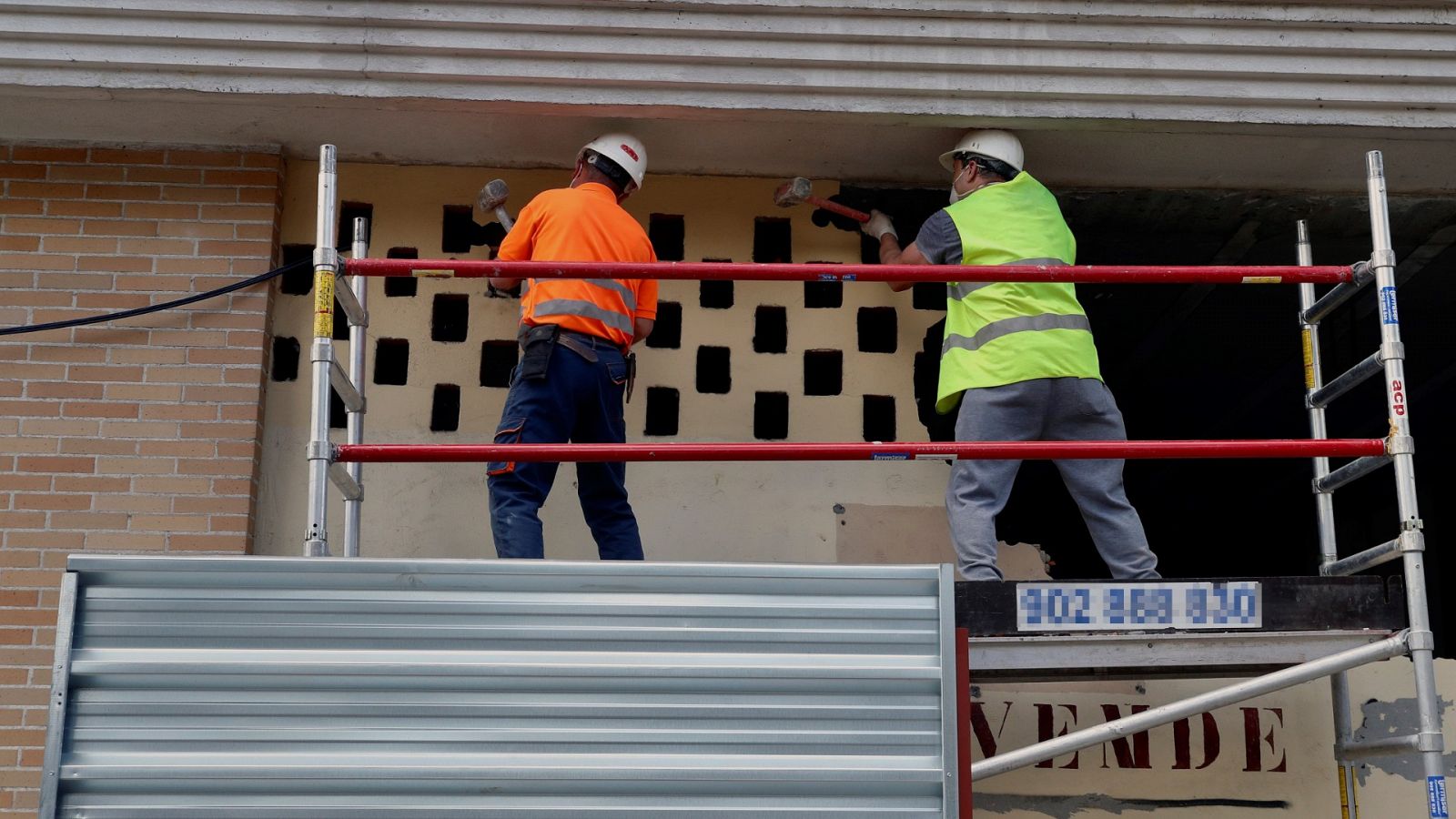Dos operarios de la construcción realizan trabajos en la fachada de un edificio.