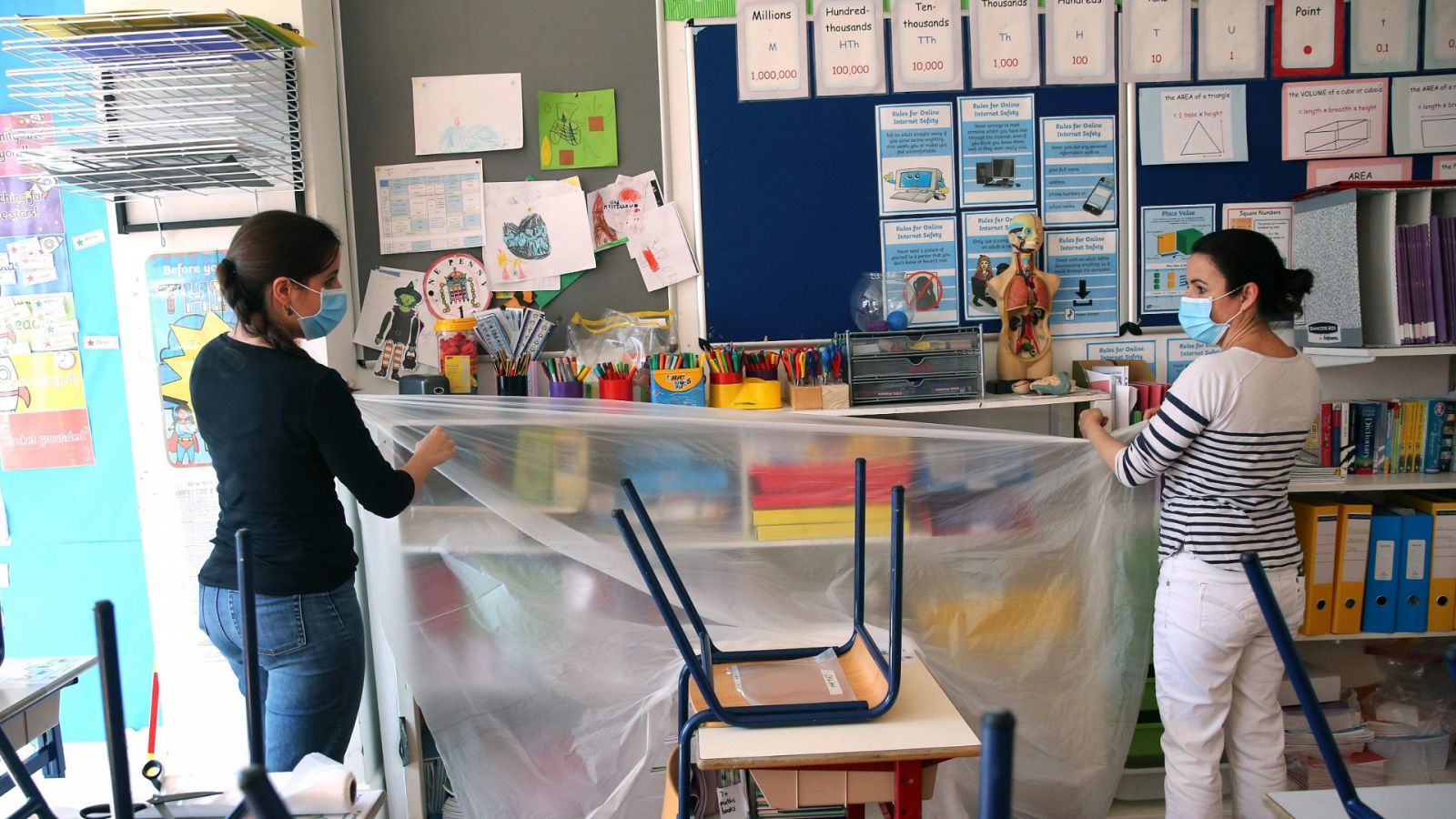 Dos profesoras cubren con plástico una estantería en un colegio de Londres.