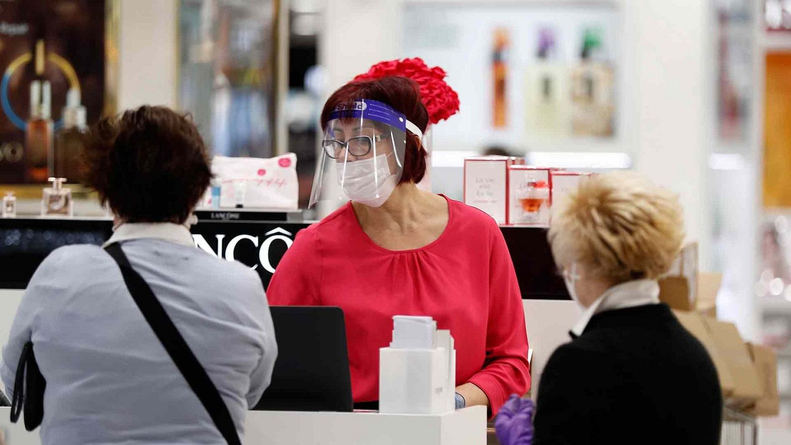 Una dependienta con mascarilla atiende a clientas que compran mascarillas en un supermercado