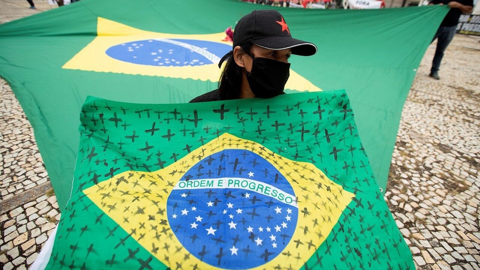 Una mujer con una bandera de Brasil con cruces por las víctimas del coronavirus