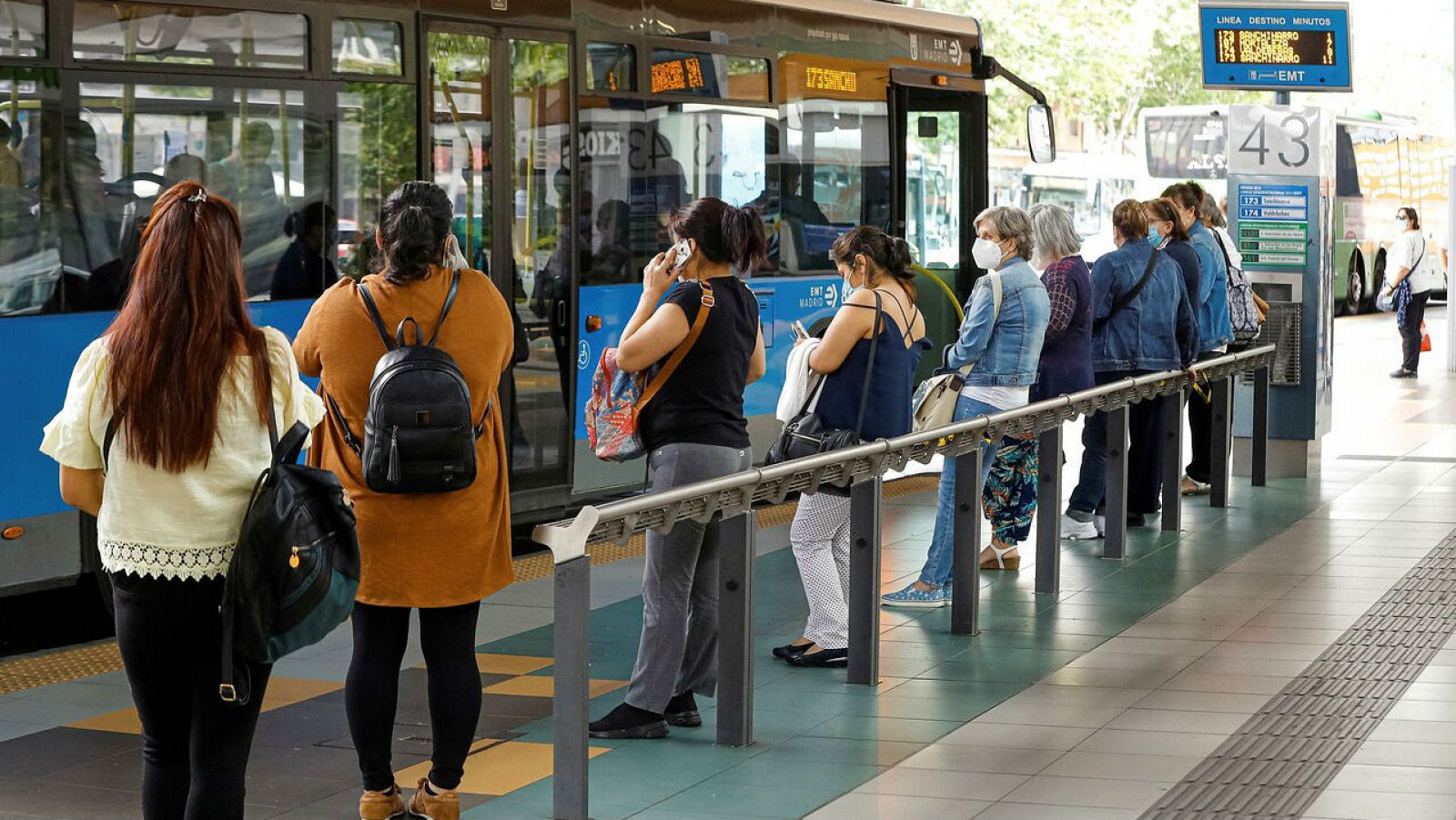 Viajeros esperan la cola del autobús en Madrid mientras miran sus teléfonos móviles.