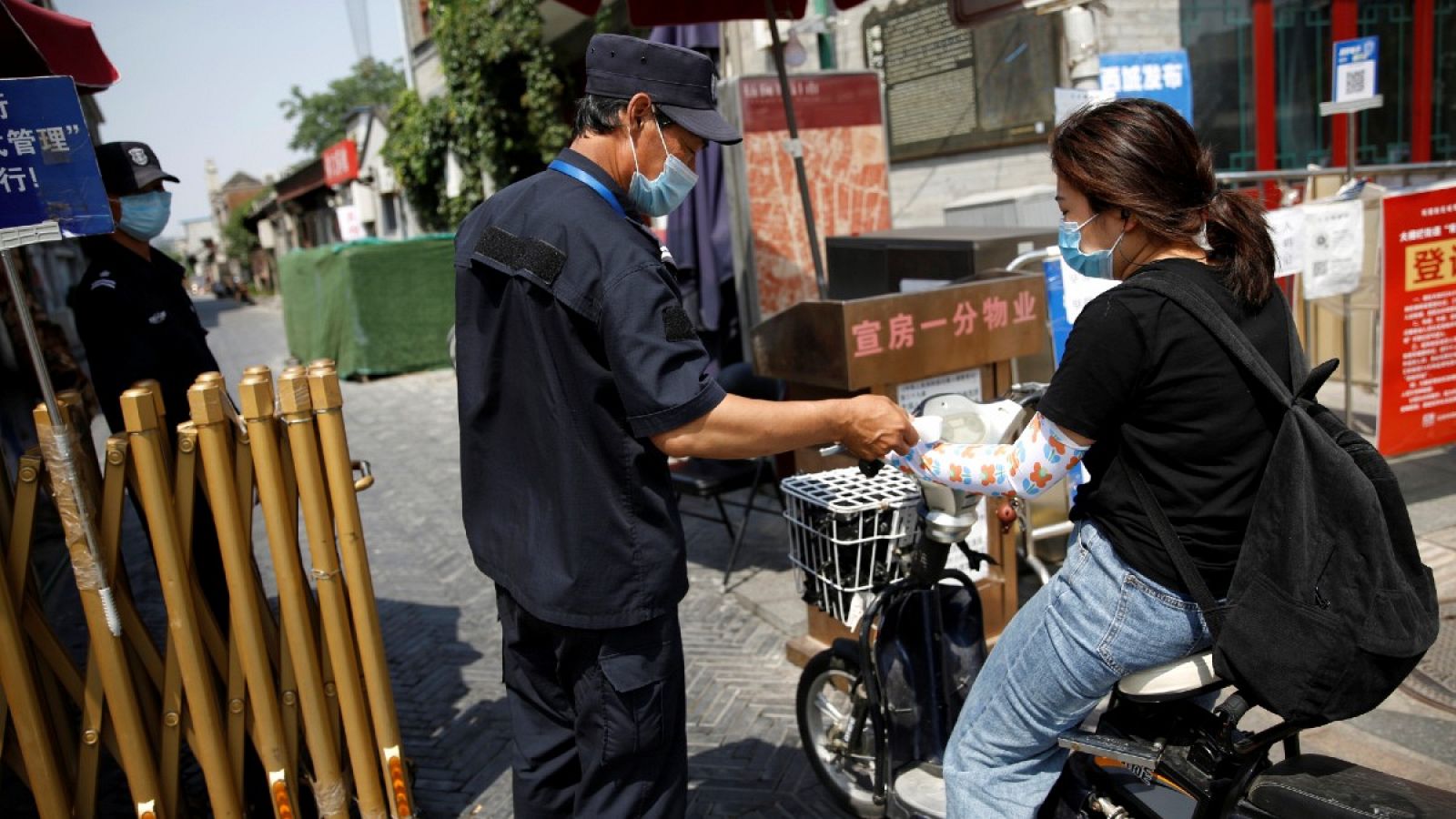 Un guardia de seguridad con mascarilla toma la temperatura de una mujer en una bicicleta en Pekín