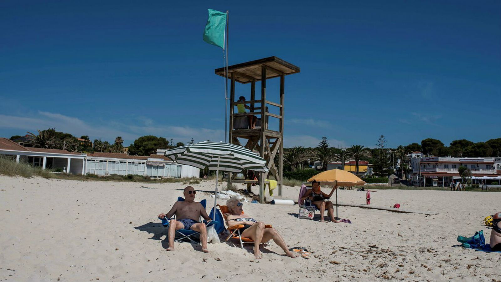 Varias personas disfrutan en la playa del primer día de la denominada "nueva normalidad" en la playa de Punta Prima, Menorca.