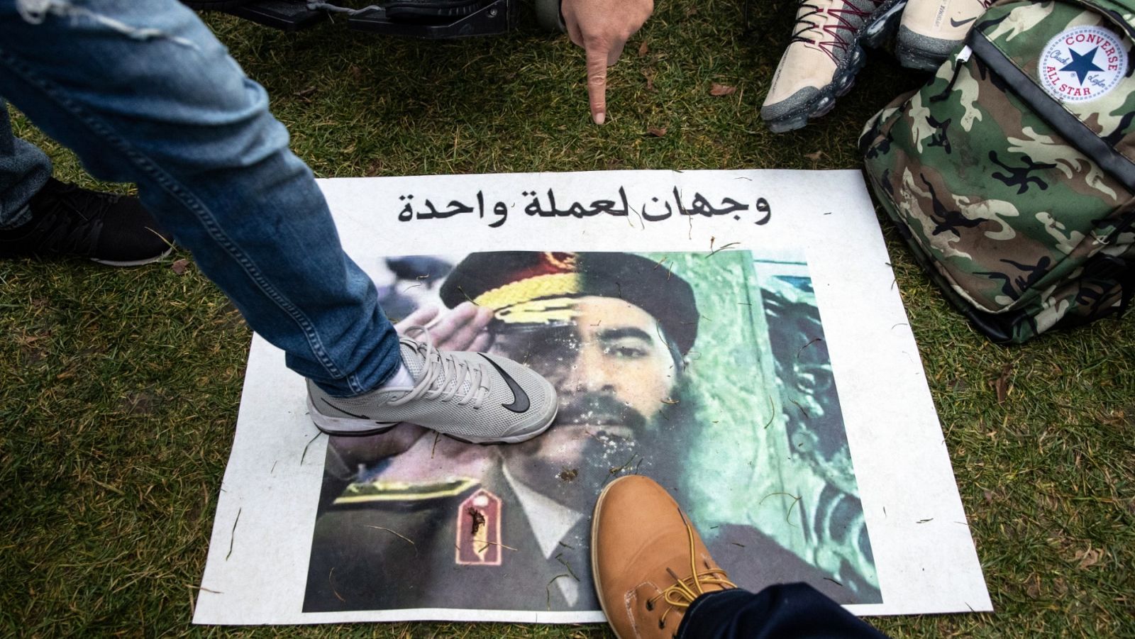 Varias personas pisan una pancarta con un retrato con una mitad del mariscal National Army Khalifa Haftar y el líder del ISIS Abu Bakr al-Baghdadi con la frase "Dos caras de la misma moneda".