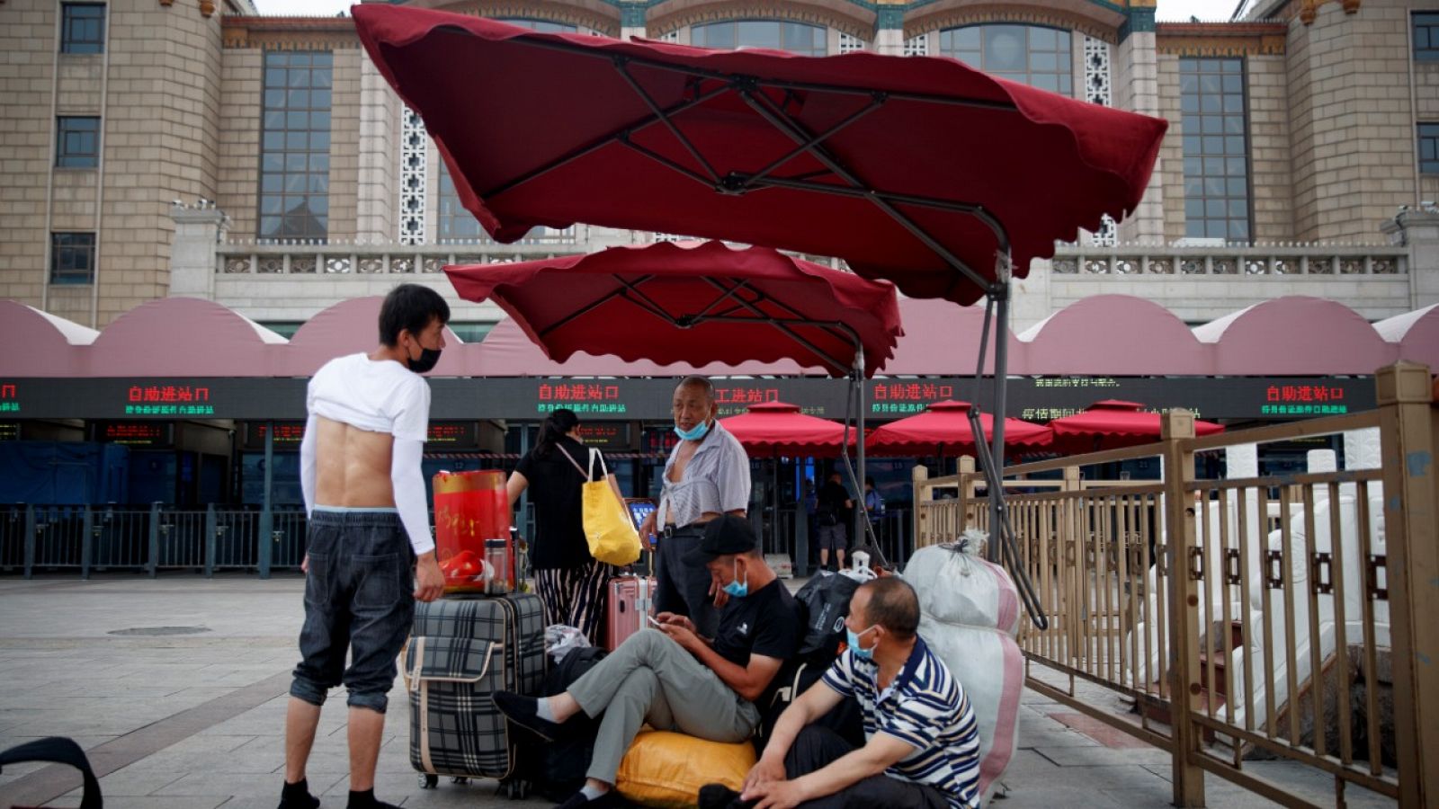 Varias personas sentadas en su equipaje en el exterior de la estación de tren de Pekín.