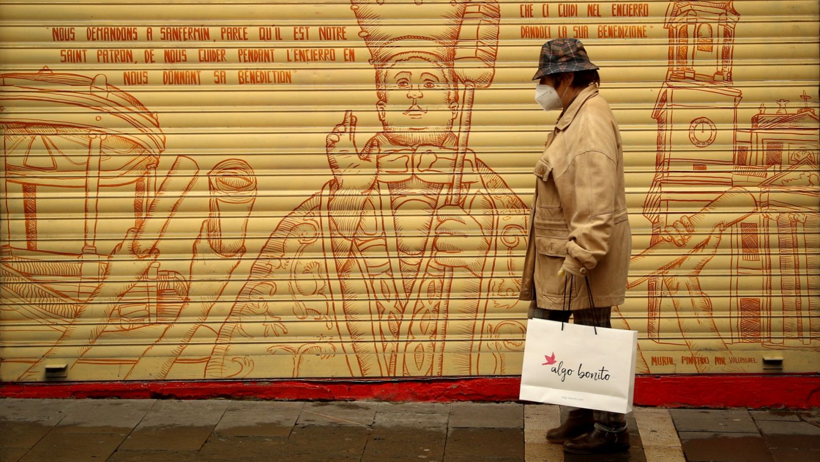 Una mujer pasa por delante de un graffiti de San Fermín en la curva de Mercderes de Pamplona