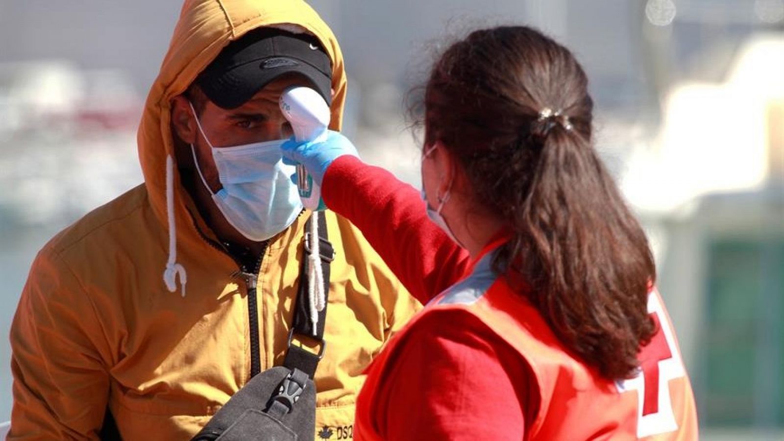Personal de Cruz Roja toma la temperatura con un termómetro de infrarrojos a un inmigrante recién llegado a puerto.