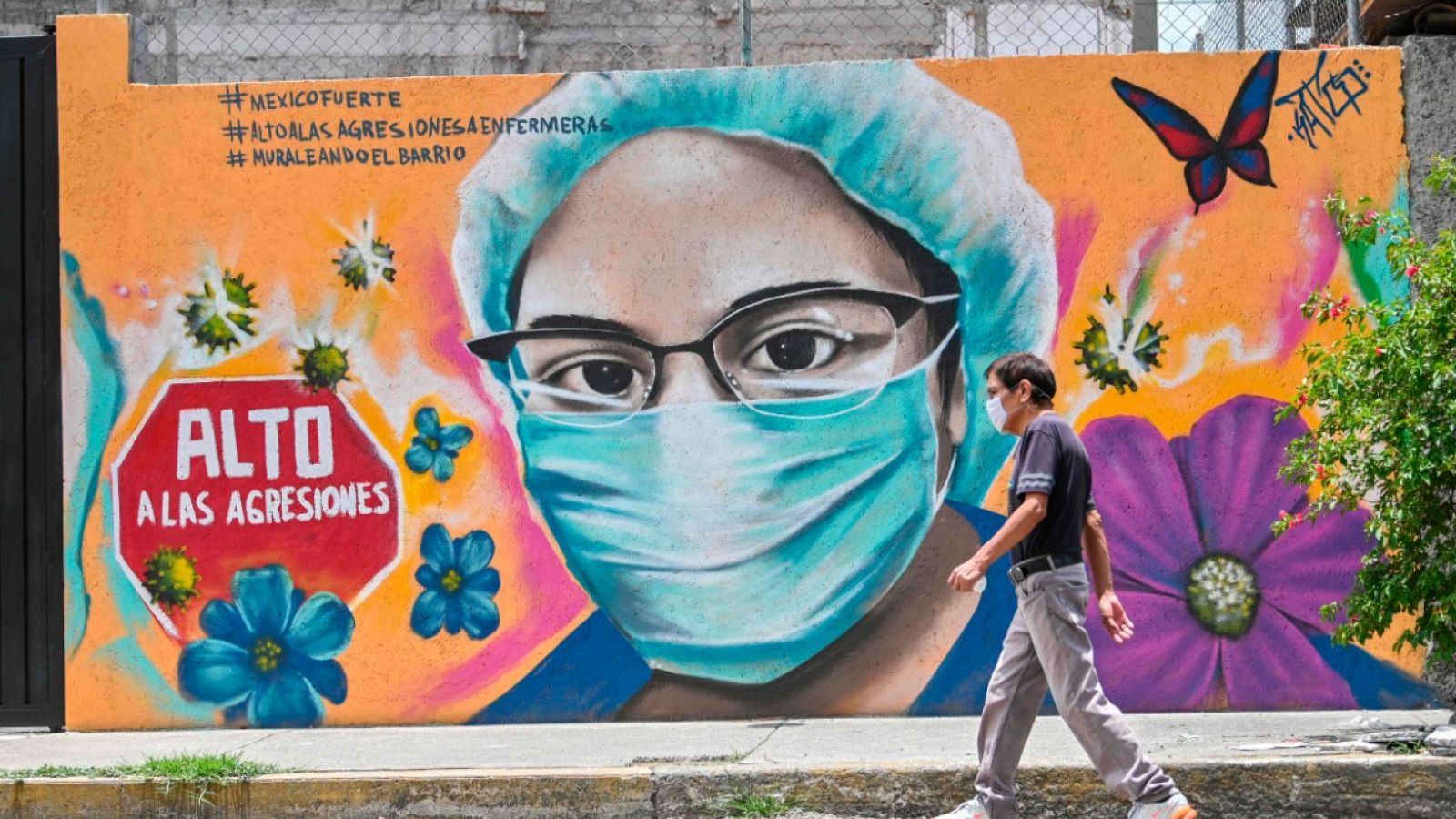 Un hombre con mascarilla pasando por delante de un mural pintado en una pared de Ciudad de México.