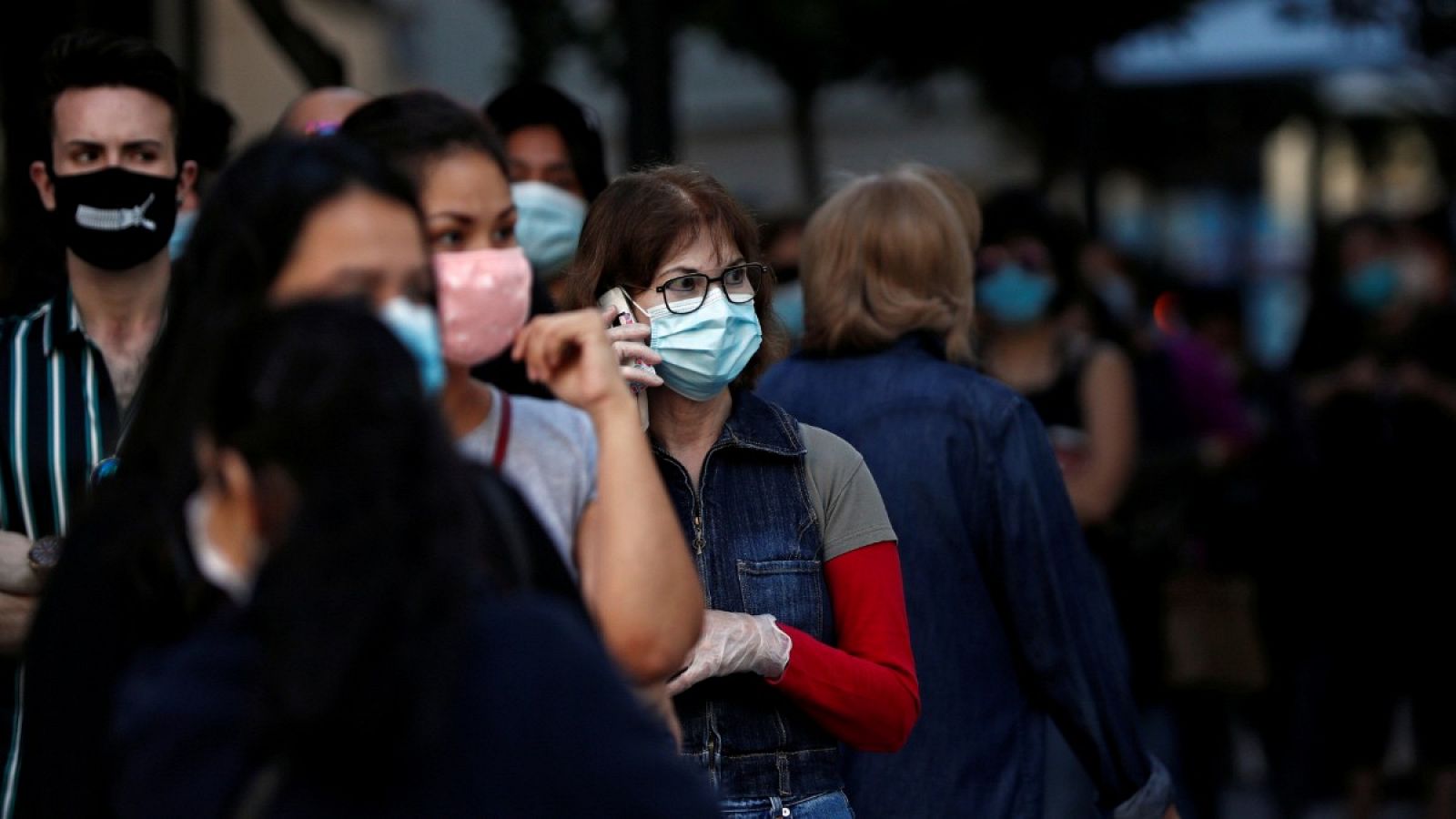 Una mujer con mascarilla y guantes habla por teléfono en la calle