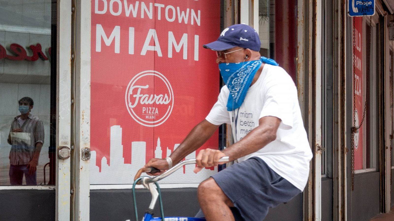 Un hombre con un pañuelo tapándole la boca y la nariz monta en bicicleta por una calle de Miami, Florida.