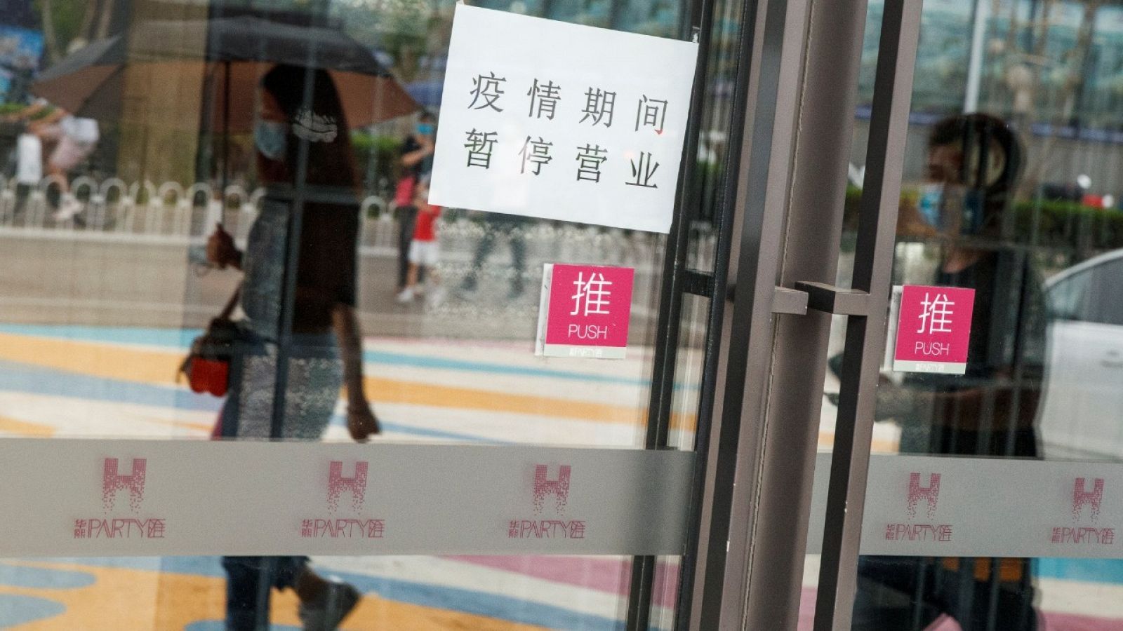 Gente reflejada en el cristal de una puerta mientras pasean por una calle de Pekín. 