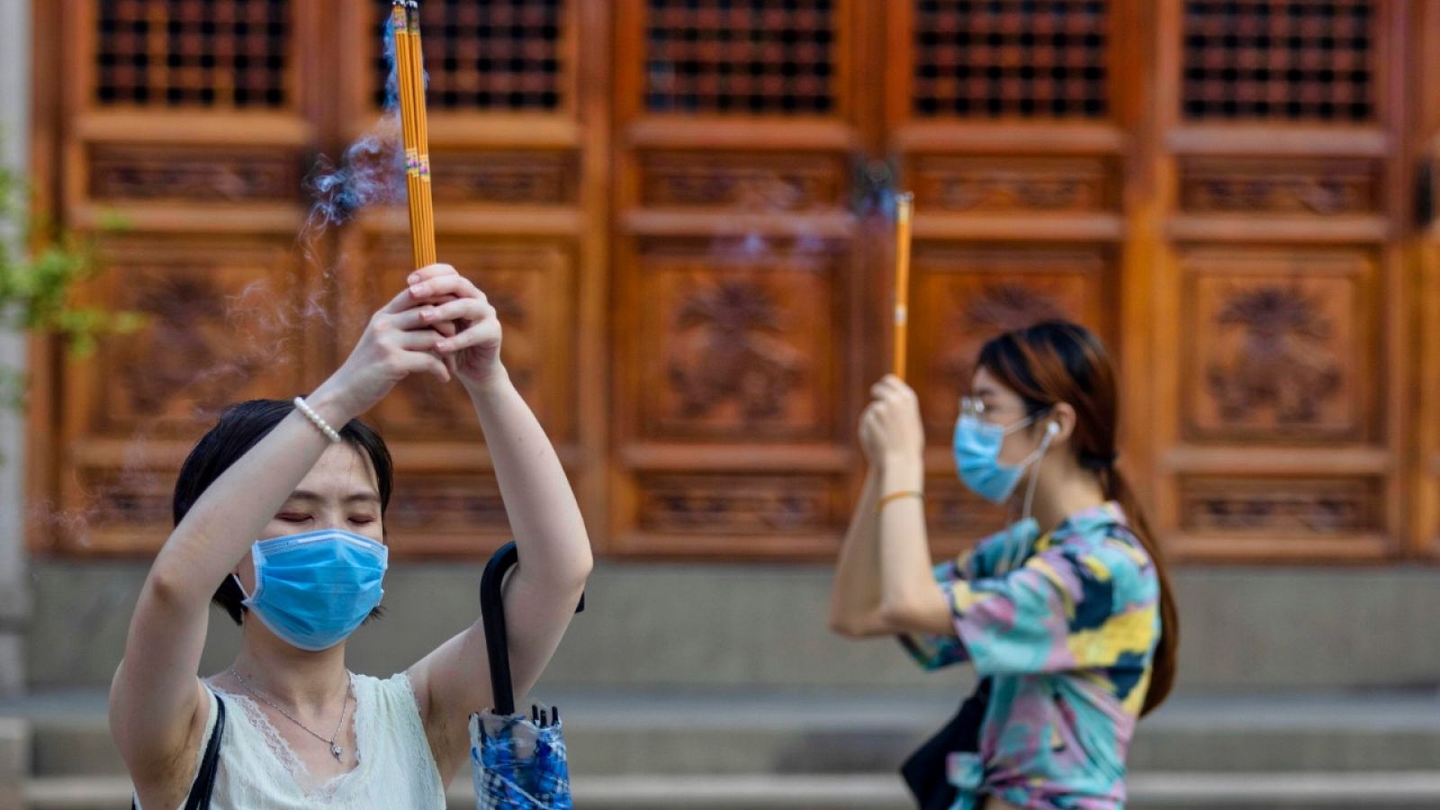 Dos mujeres con mascarilla sujetando varillas de incienso en un templo budista en Shanghái, China.