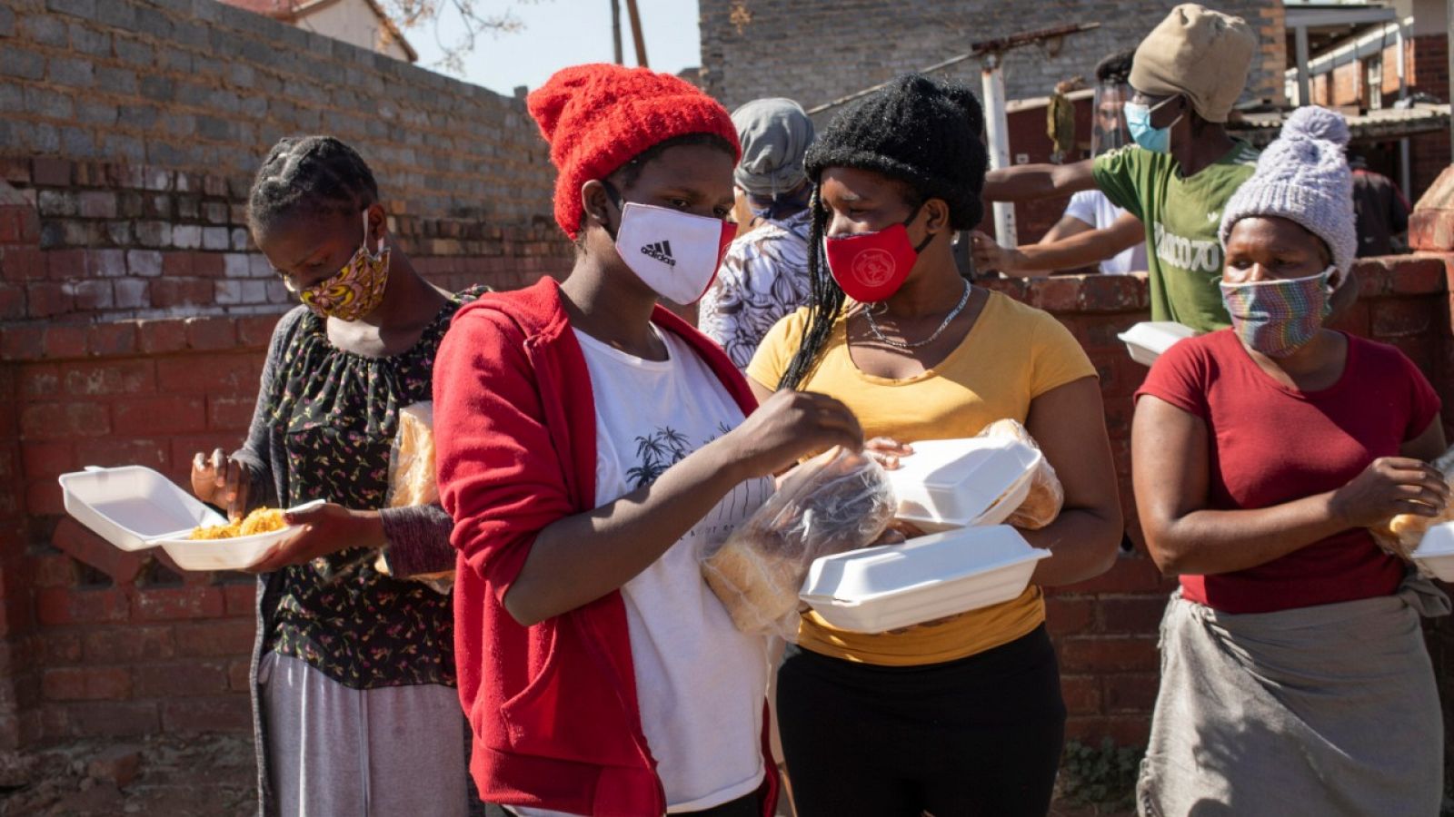 Mujeres con mascarilla recibiendo pan y alimentos en Johannesburgo, Sudáfrica.