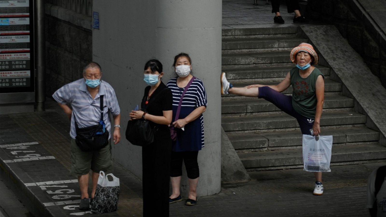 Varias personas con mascarilla esperando al autobús en una parada de Pekín. 