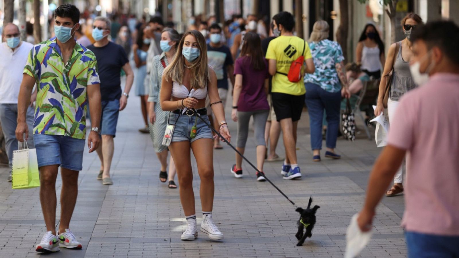 Una chica pasea con su perro en un transitada calle de Madrid