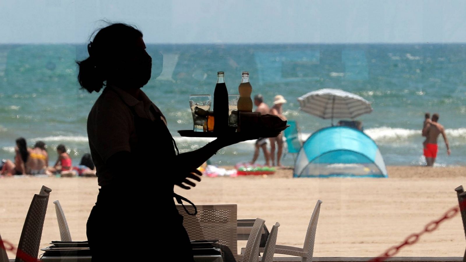 Una camarera lleva una bandeja con bebidas en un restaurante de la playa de la Malvarrosa, en Valencia