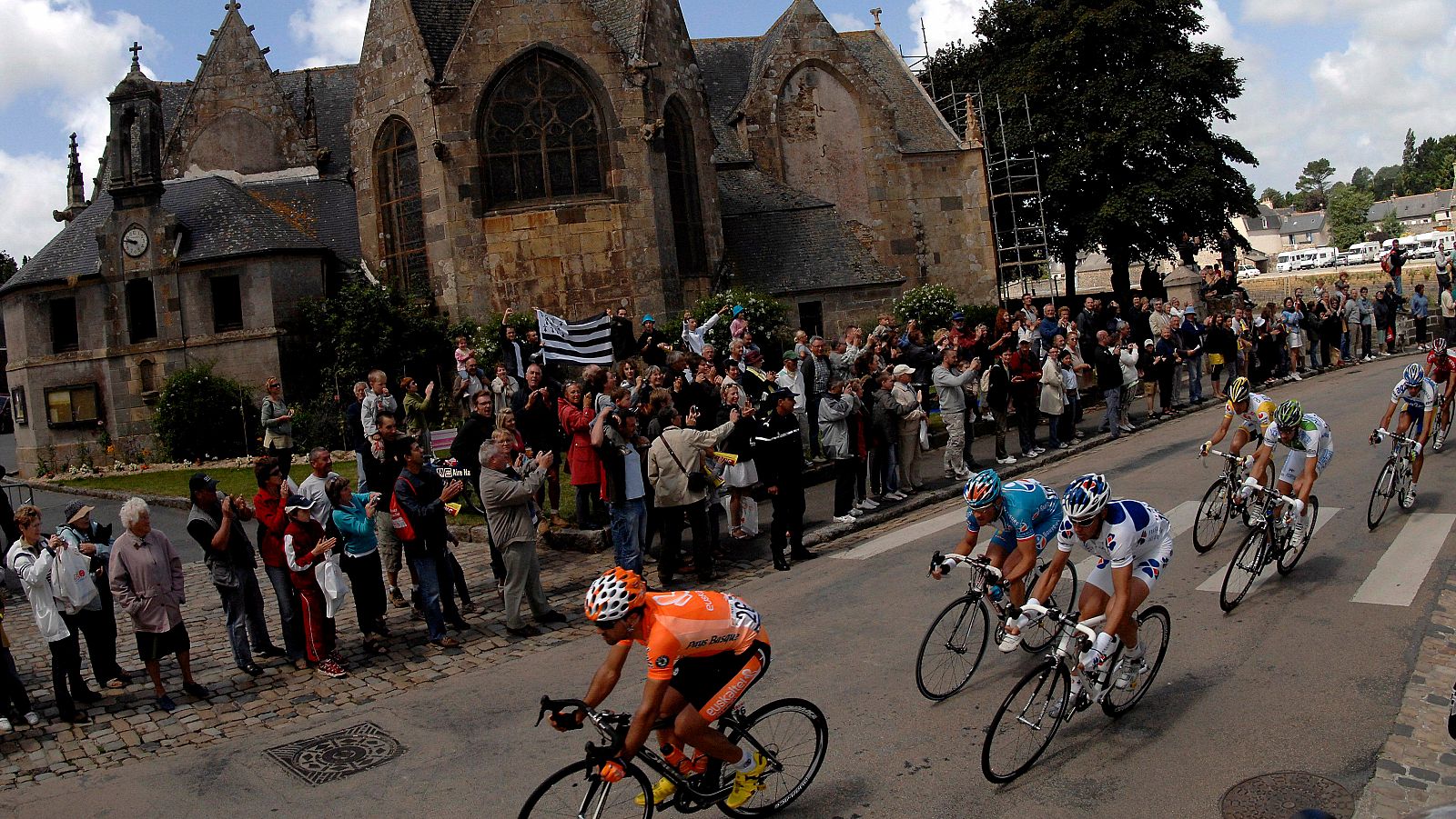 Un grupo de aficionados con una bandera bretona al paso de los ciclistas por delante de una iglesia durante el Tour 2008