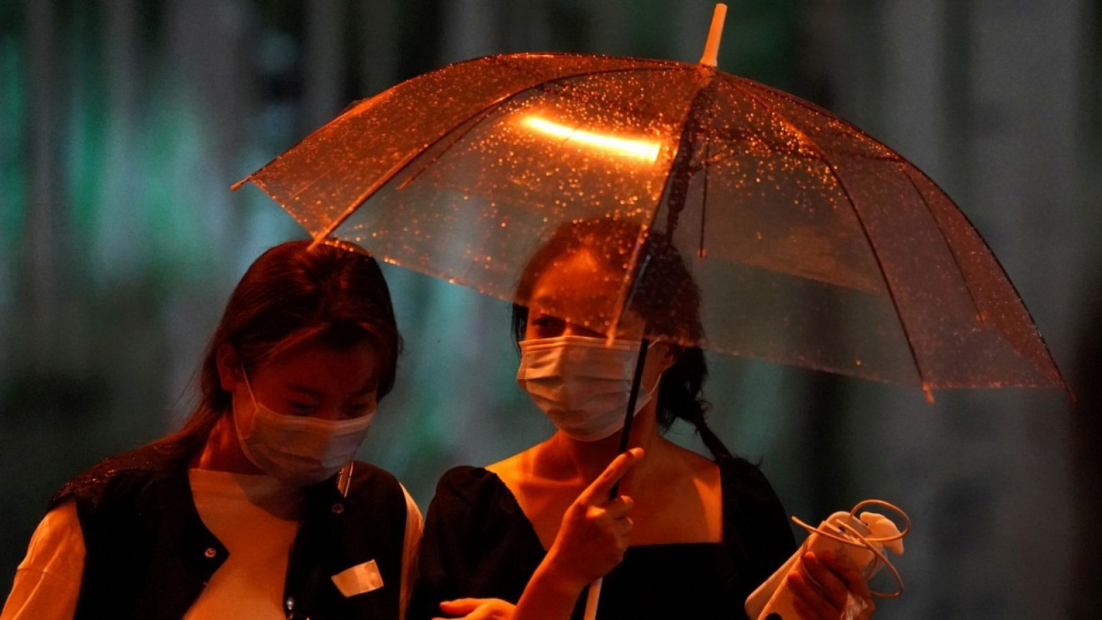Dos mujeres con mascarillas caminando con un paraguas bajo la lluvia por una calle de Pekín, China.  
